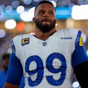 Los Angeles Rams defensive tackle Aaron Donald wearing a white and royal blue number 99 jersey on the football field under bright stadium lights.