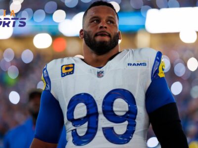 Los Angeles Rams defensive tackle Aaron Donald wearing a white and royal blue number 99 jersey on the football field under bright stadium lights.